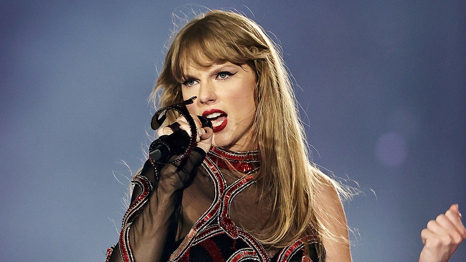 Taylor Swift con un mono de malla negro y rojo oscuro canta en su micrófono durante la gira The Eras