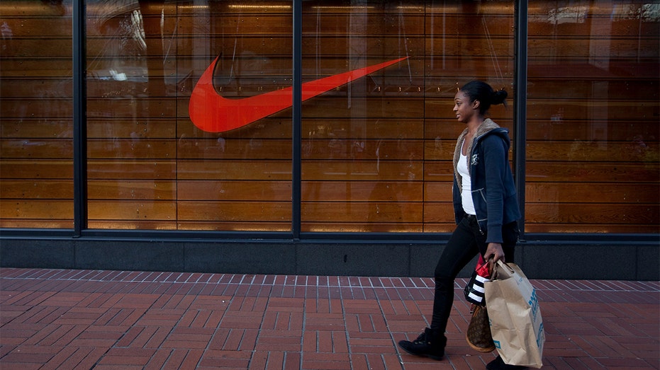 A woman walks with shopping bags in front of a Nike store.