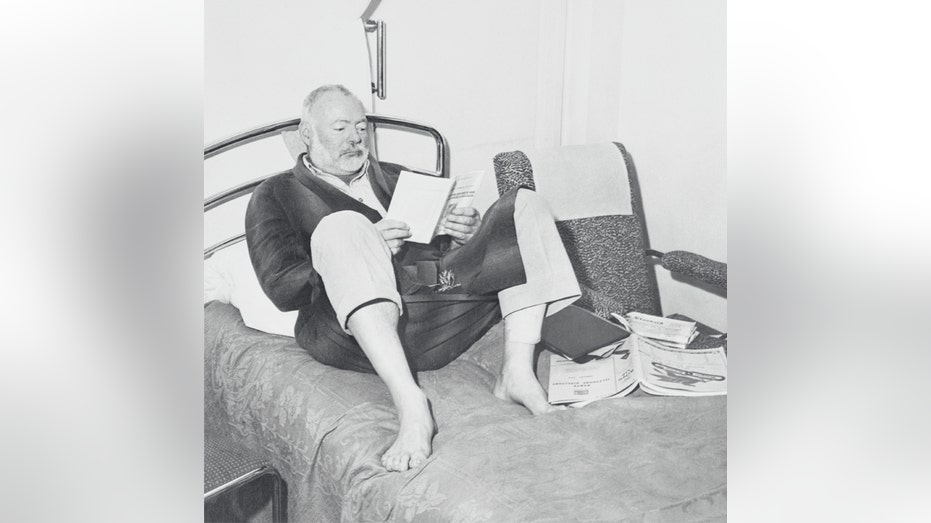 Ernest Hemingway reads in his recovery bed.