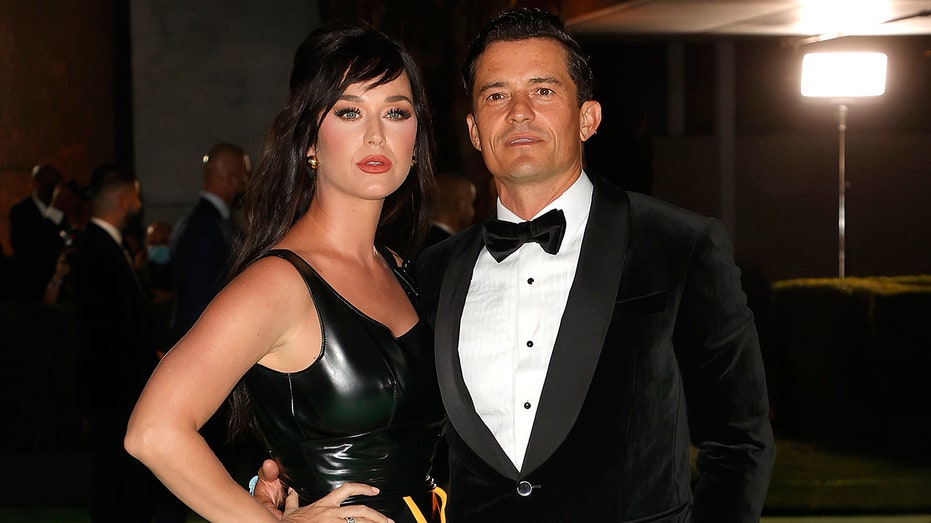 Katy Perry in a leather dress poses with Orlando Bloom in a traditional tuxedo