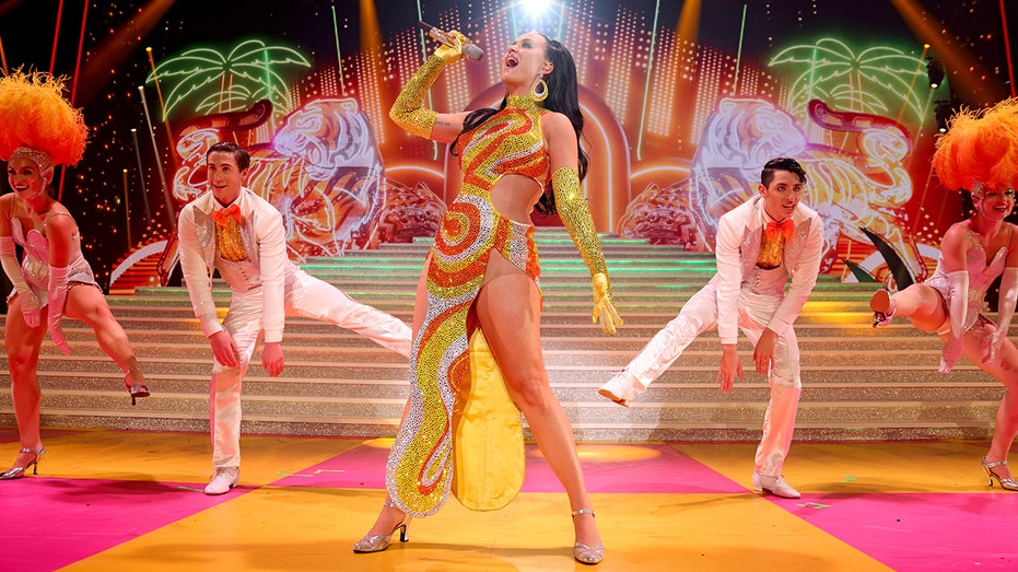 Katy Perry in a 70s inspired yellow and orange outfit singing on stage in Las Vegas