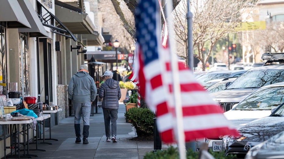 pedestrians walk in front of flag