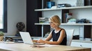 Businesswoman using laptop at desk. Confident female professional is working in textile factory. Executive is with short brown hair.