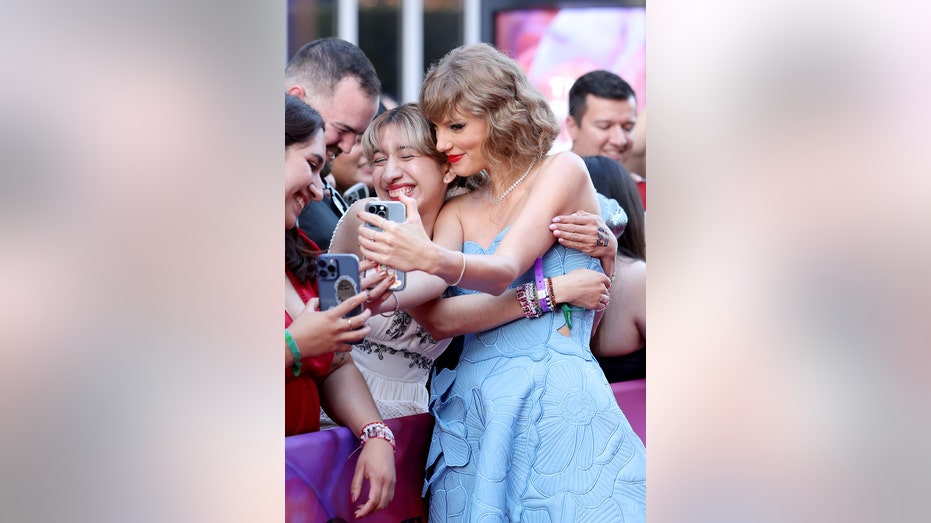 Taylor Swift in a blue strapless dress being embraced by fans