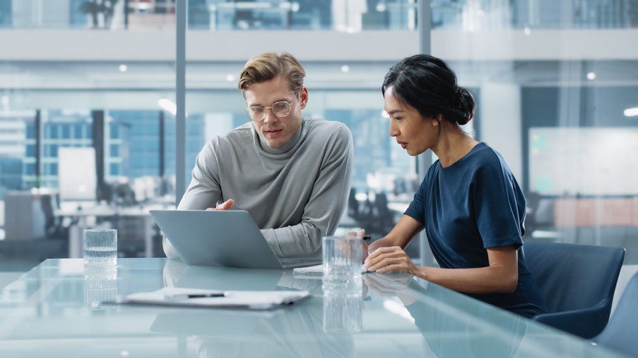 two people sitting and looking at a laptop