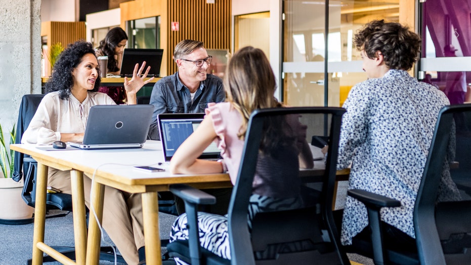 four people sitting at an office table talking