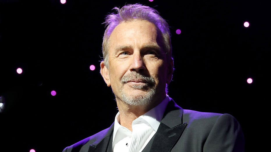 Kevin Costner wears black suit on stage at awards show