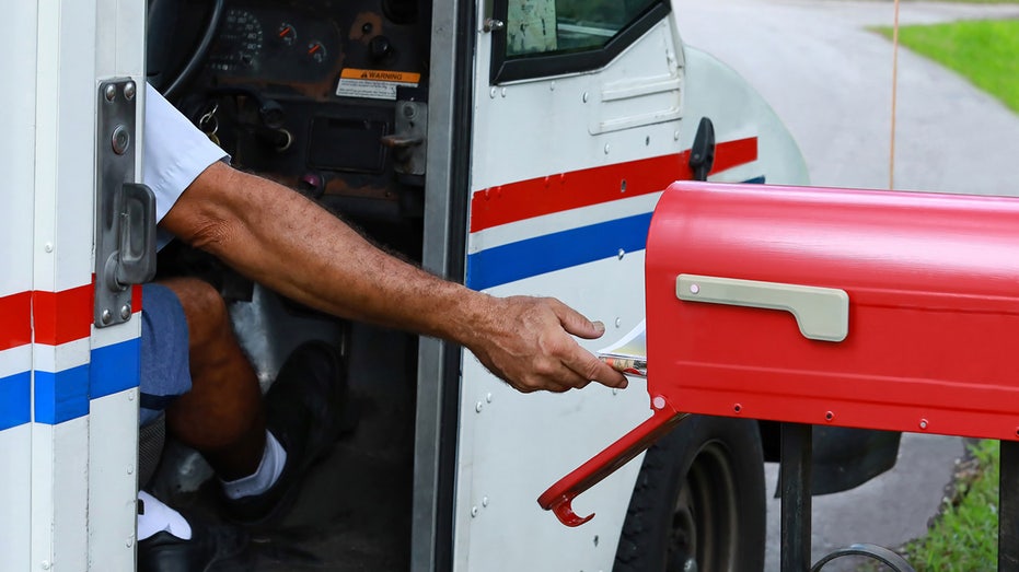 Postal worker putting mail in mailbox