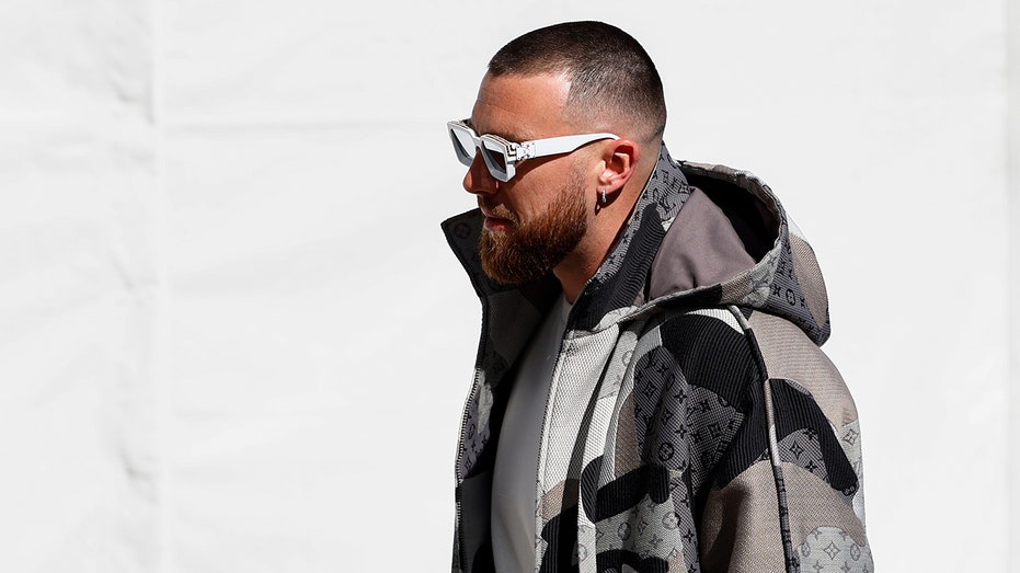 Travis Kelce walking in designer jacket and sunglasses