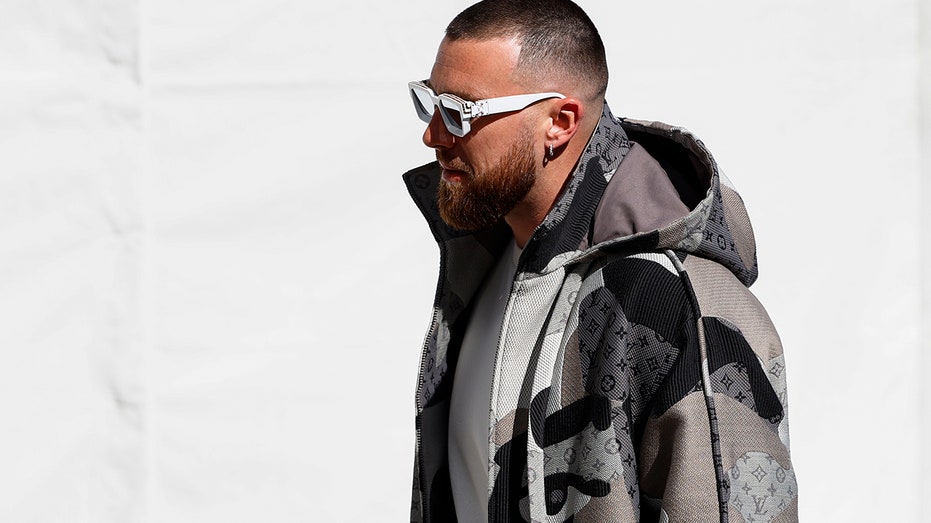 Travis Kelce walking in designer jacket and sunglasses
