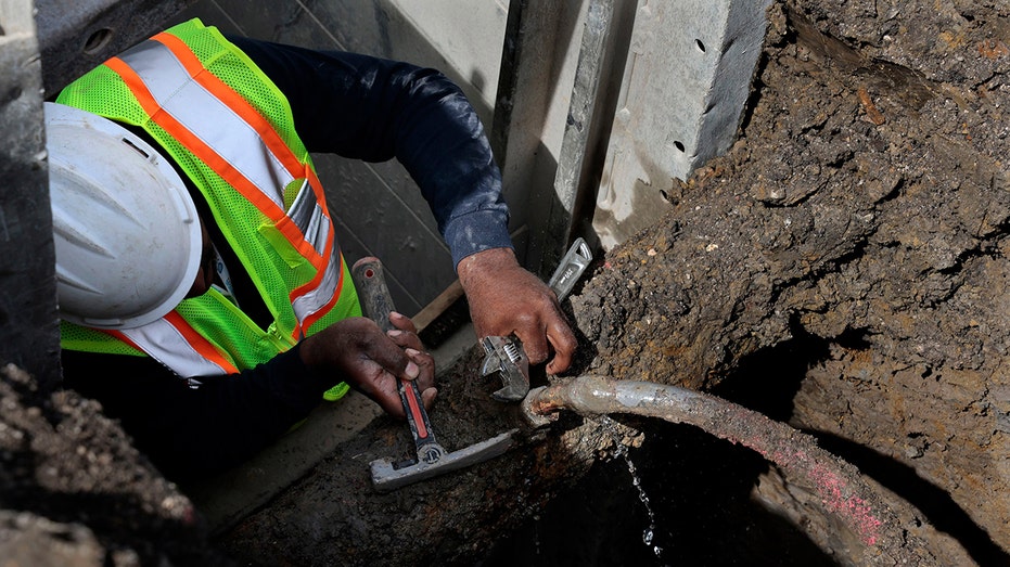 A sewer worker repairs a leaking lead pipe