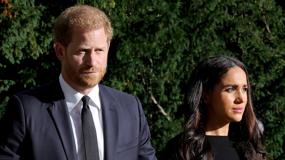 Prince Harry wearing a dark grey suit and Meghan Markle wearing a black dress as they both look serious