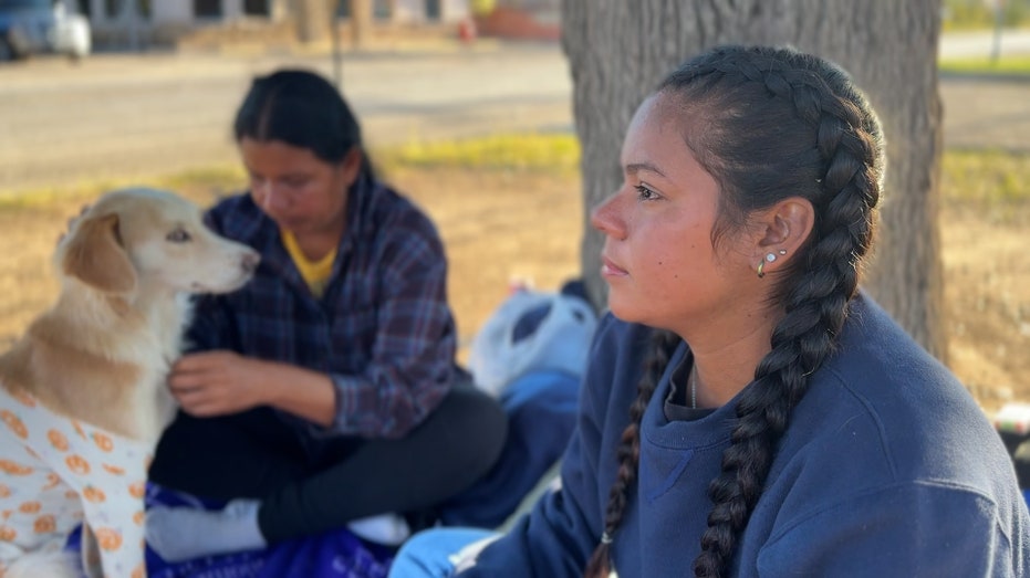 a migrant mom and daughter sit outside with their dog