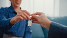 Close up of young Asian woman sign contract getting keys on sofa in living room at home.