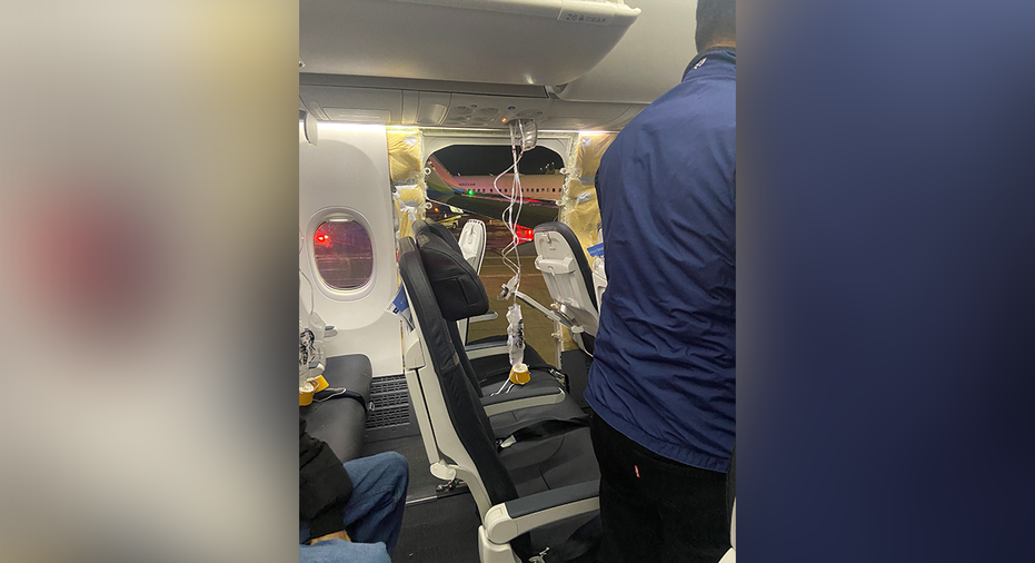 Passenger oxygen masks hang from the roof next to a missing window and a portion of a side wall of an Alaska Airlines Flight 1282.