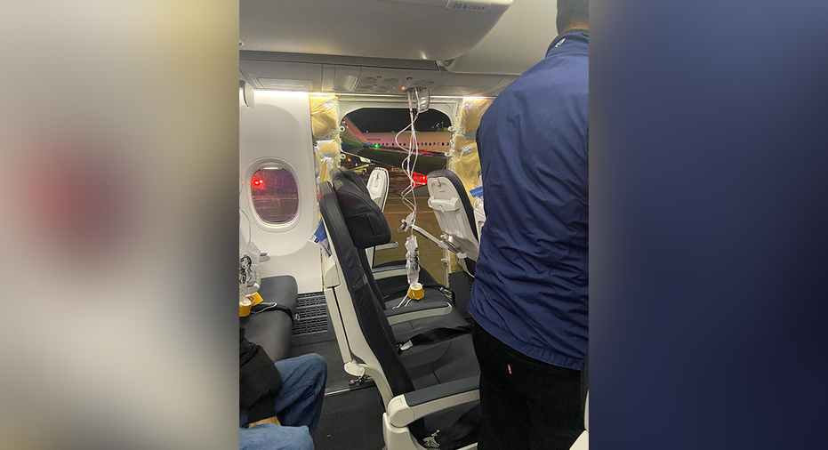 Passenger oxygen masks hang from the roof next to a missing window and a portion of a side wall of an Alaska Airlines Flight 1282.