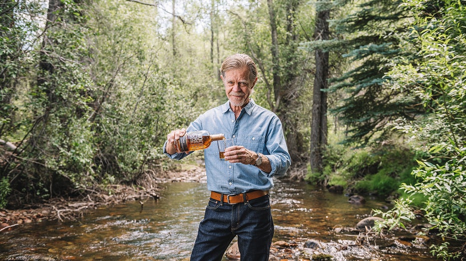 William H. Macy pouring whiskey in a glass outdoors