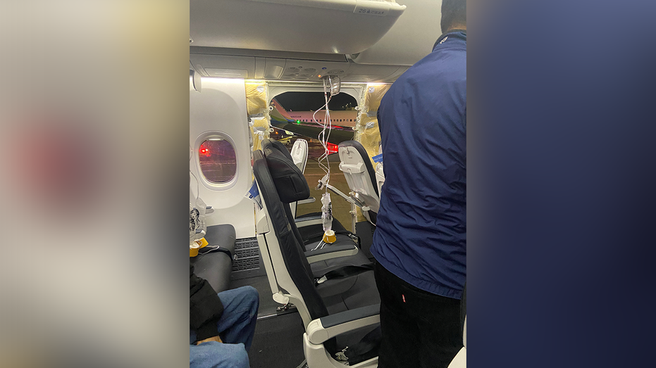 Passenger oxygen masks hang from the roof next to a missing window and a portion of a side wall of Alaska Airlines Flight 1282.