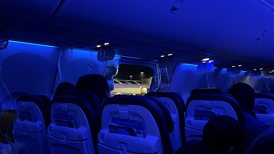 Personas sentadas en un avión junto a una ventana faltante y parte de la pared lateral del vuelo 1282 de Alaska Airlines.