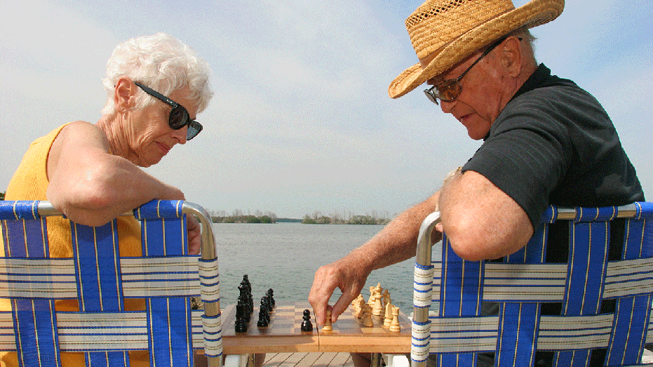 A senior couple playing chess on a beach