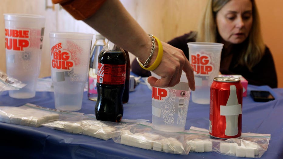 A display of sugary drinks shows sugar content in large soda cups