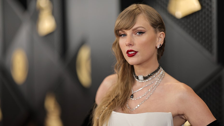Taylor Swift with multiple necklaces and a white gown looks serious on the carpet at the Grammys