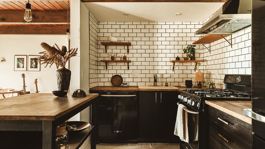 A kitchen with black cupboards and white brick.