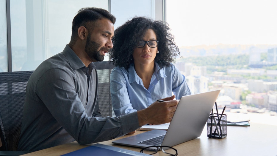 Two people look at a laptop screen.
