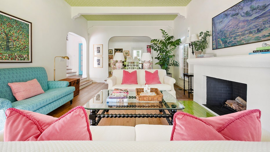 A living room with white couches, a fire place and pink pillows.