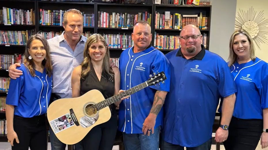 Adults standing, smiling next to Taylor Swift guitar