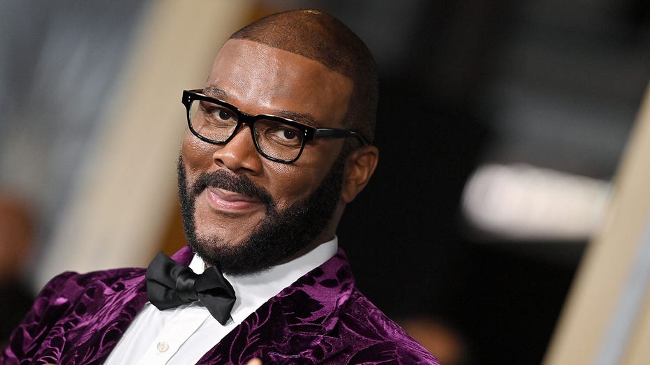 Tyler Perry in a velvet purple tuxedo soft smiles ont he carpet