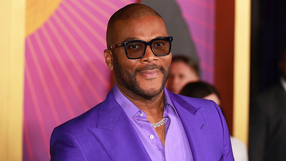 Tyler Perry in a bright purple jacket and lilac purple shirt on the carpet with black tinted glasses