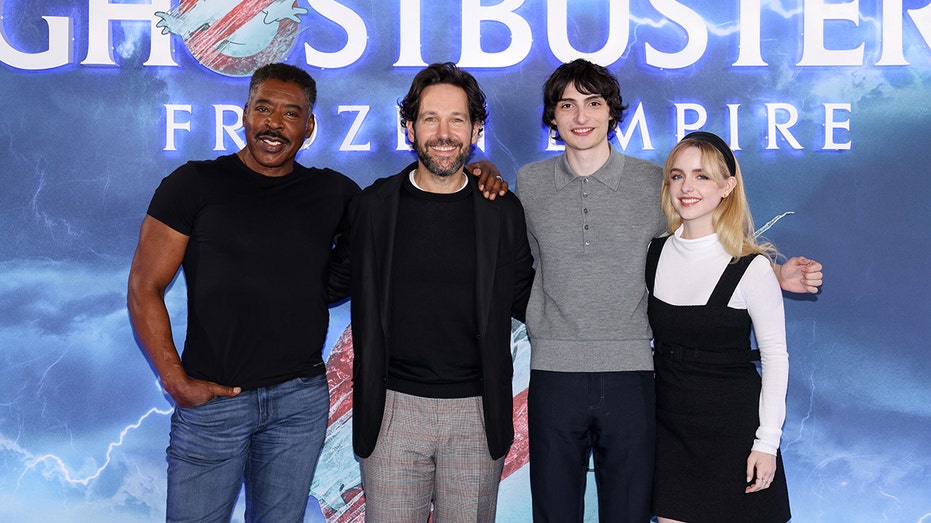 Ernie Hudson, Paul Rudd, Finn Wolfhard, McKenna Grace posing in front of Ghostbusters: Frozen Empire signage