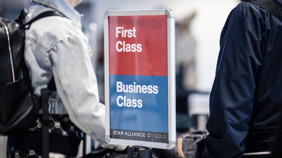 Airport travelers next to sign reading "First Class/Business Class"