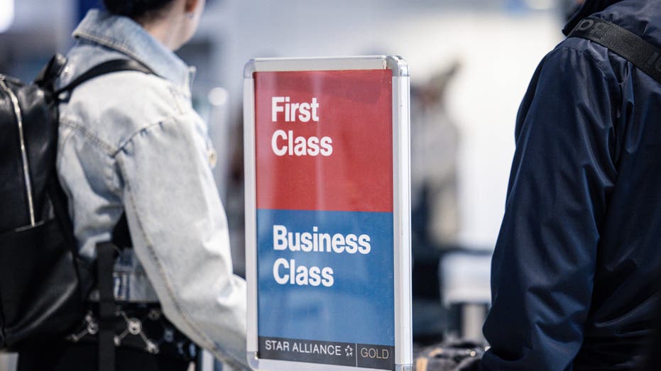 Airport travelers next to sign reading "First Class/Business Class"