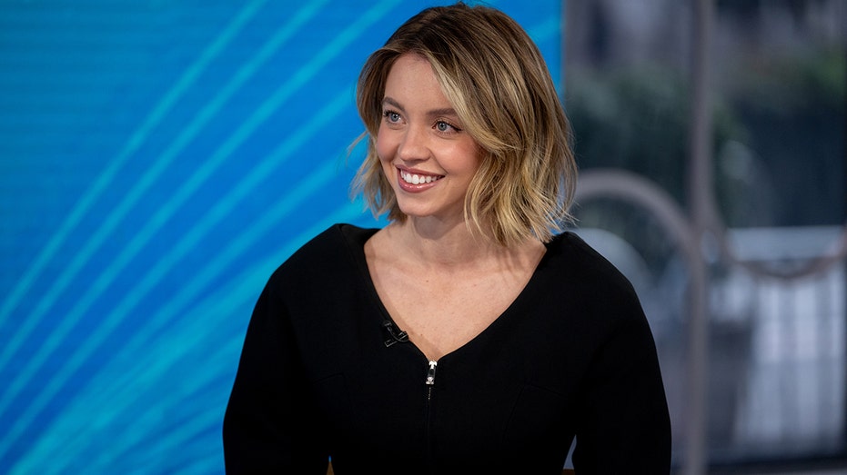 Sydney Sweeney in a black dress in front of a blue background.