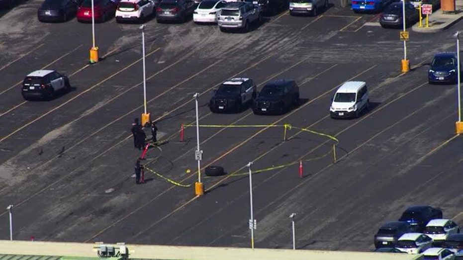 Police cars in parking lot, yellow tape and officers around tape