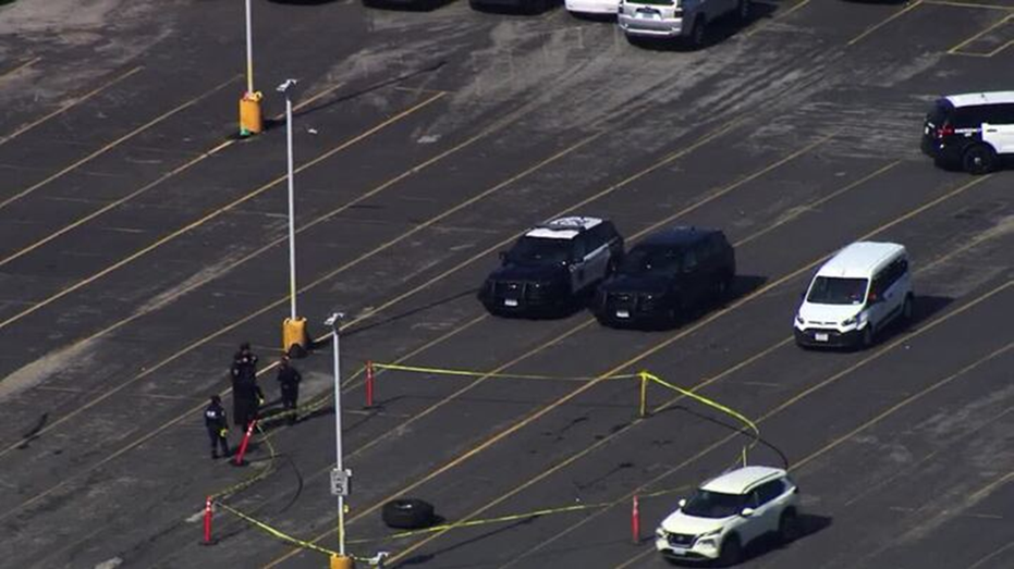 Police cars in parking lot, yellow tape and officers around tape