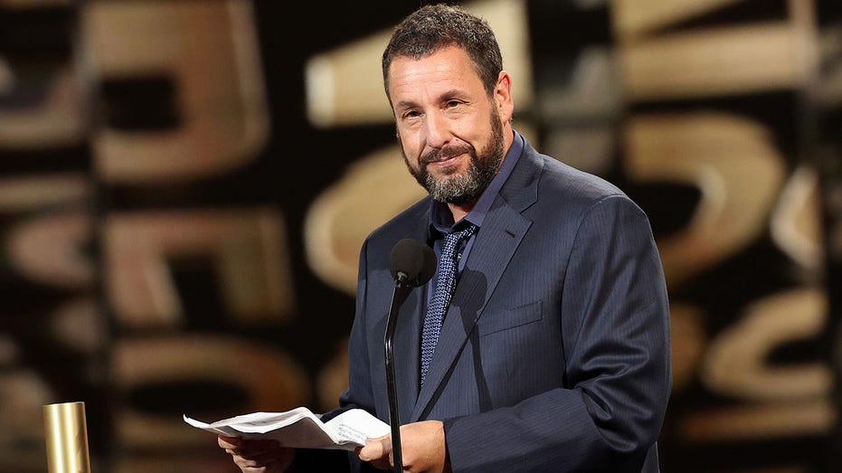 Adam Sandler stands behind a floating microphone at the People's Choice Awards holding a large wad of paper