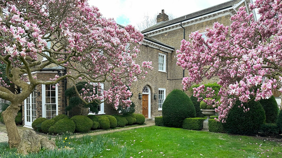 A light brown home with cherry blossoms and green grass in front.