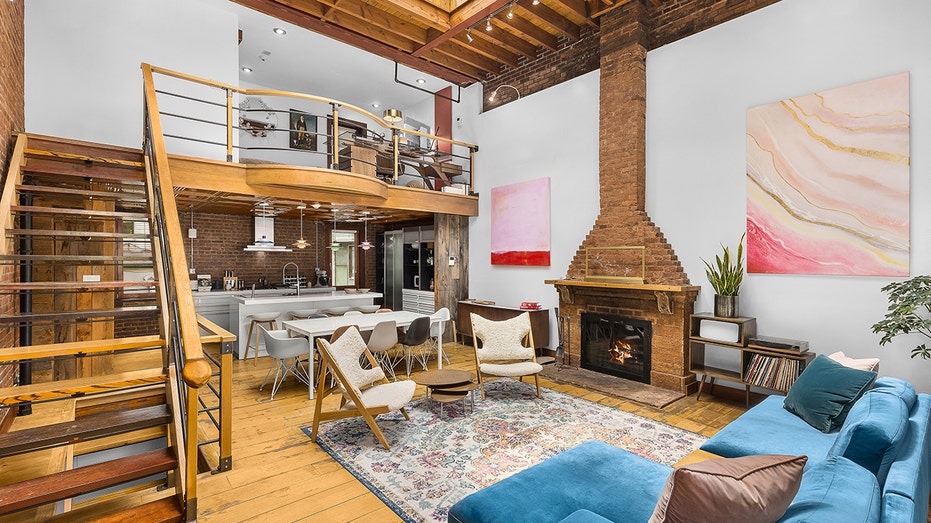 A living room with stairs, a fireplace, a blue couch and high ceilings.