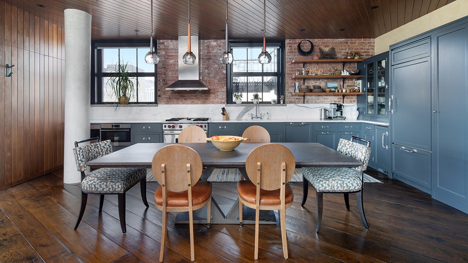 A kitchen with blue cabinets and wooden chairs around the table.