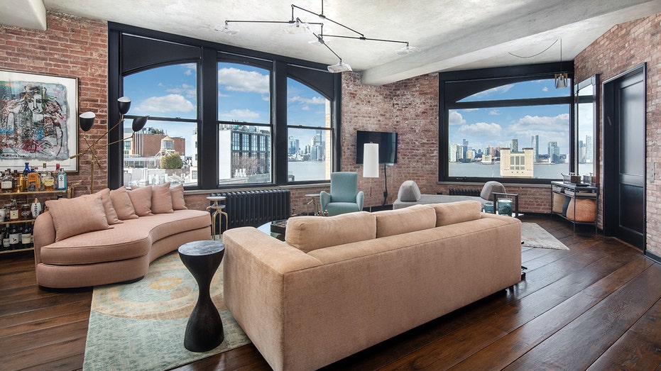 A spacious living room with big windows and tan couches.