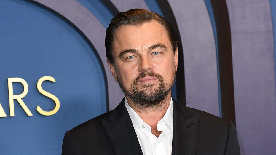 Leonardo DiCaprio in a black suit and white shirt looks stoic on the carpet