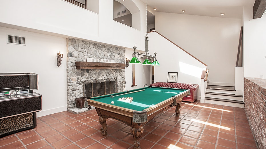 Large wood pool table with green felt in front of a large staircase and big stone fireplace at Richard Pryor's old home