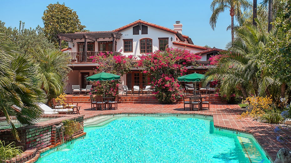 Large pool with pink flowers surrounding the property and green umbrellas on the large patio at Richard Pryor's old home