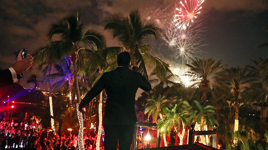 The silhouette of Sean "Diddy" Combs as he watches over a crowd of people at his house, with fireworks in the background.