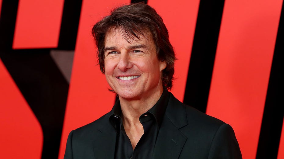 Tom Cruise in a black shirt and blazer smiles on the carpet for "Mission: Impossible - Dead Reckoning Part One"
