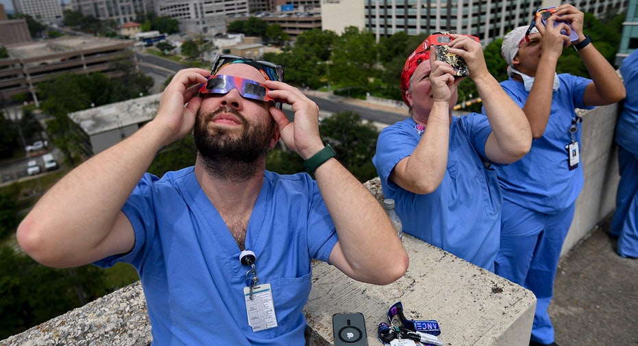Jared Kirk, left, a surgical tech at Dell Seton Medical Center, views the early stages of the solar eclipse on the top floor of the hospital’s parking garage