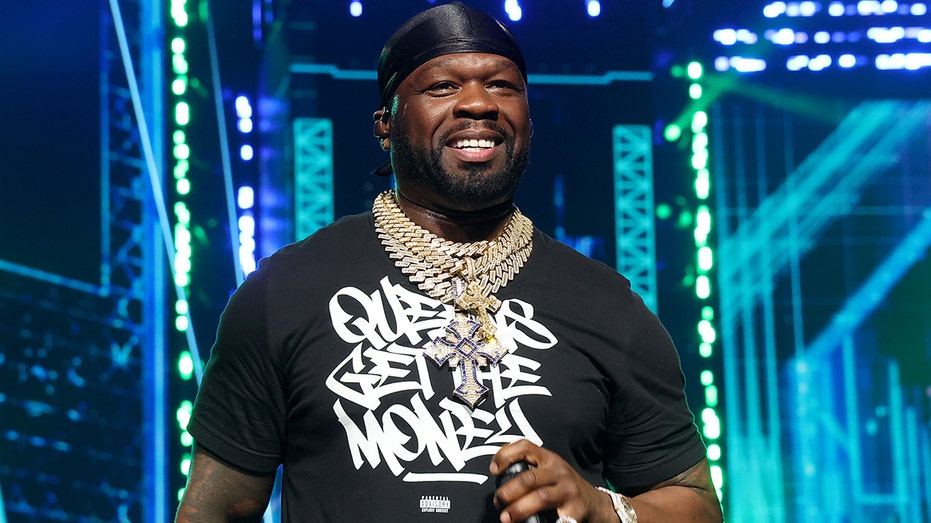 Rapper 50 Cent on stage in a black shirt with white writing.